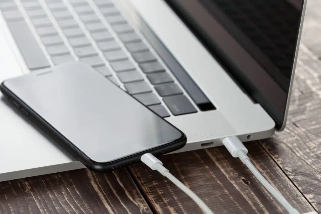 Close-up of white USB cable connecting phone and laptop.