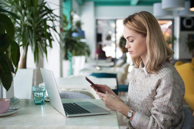 Serious woman looking at her cellphone, laptop on the table