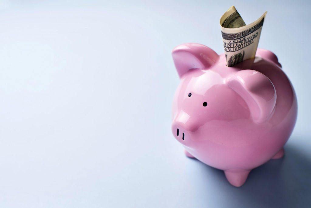 High angle view of a pink ceramic piggy bank with a dollar bill in the slot over a grey background with copyspace.