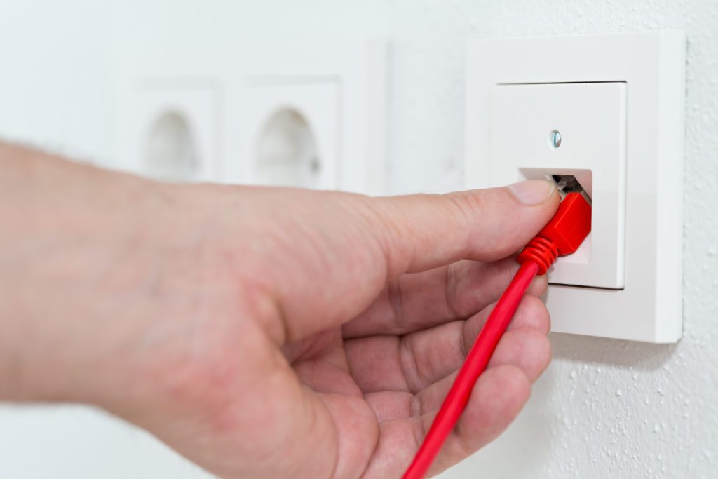 Man plugs red network cable in wall outlet.