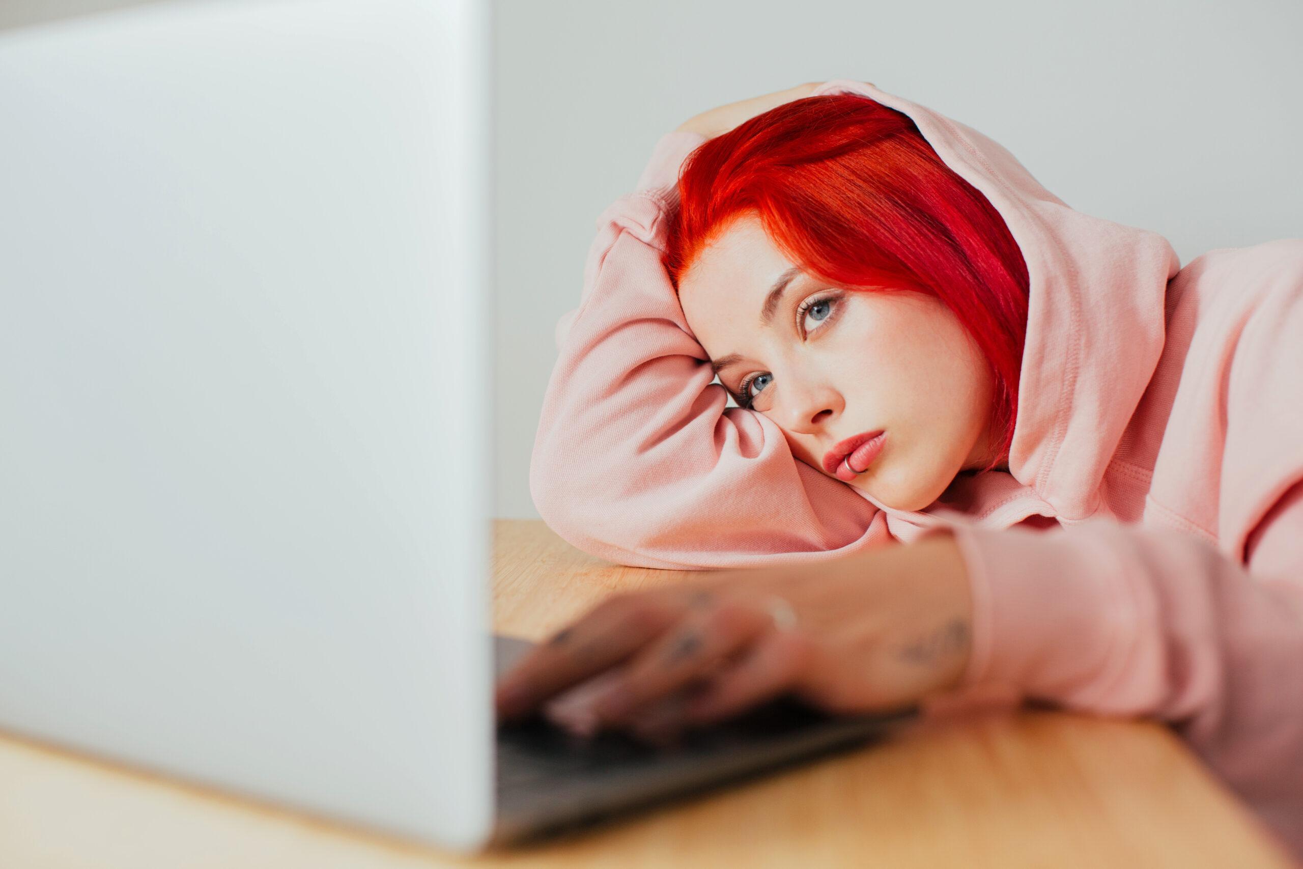 Retrato de una adolescente aburrida acostada en el escritorio usando una computadora portátil para navegar por internet