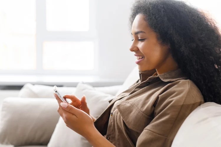 Young woman using trendy smartphone sitting on the sofa at home.
