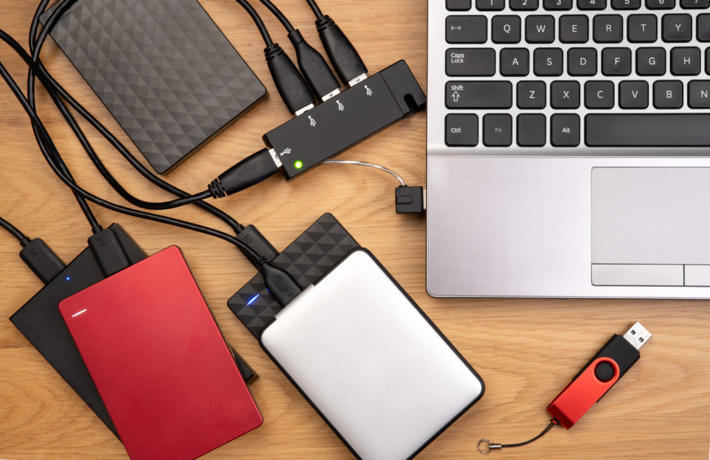 External hard drives connected to a laptop on wooden desk.