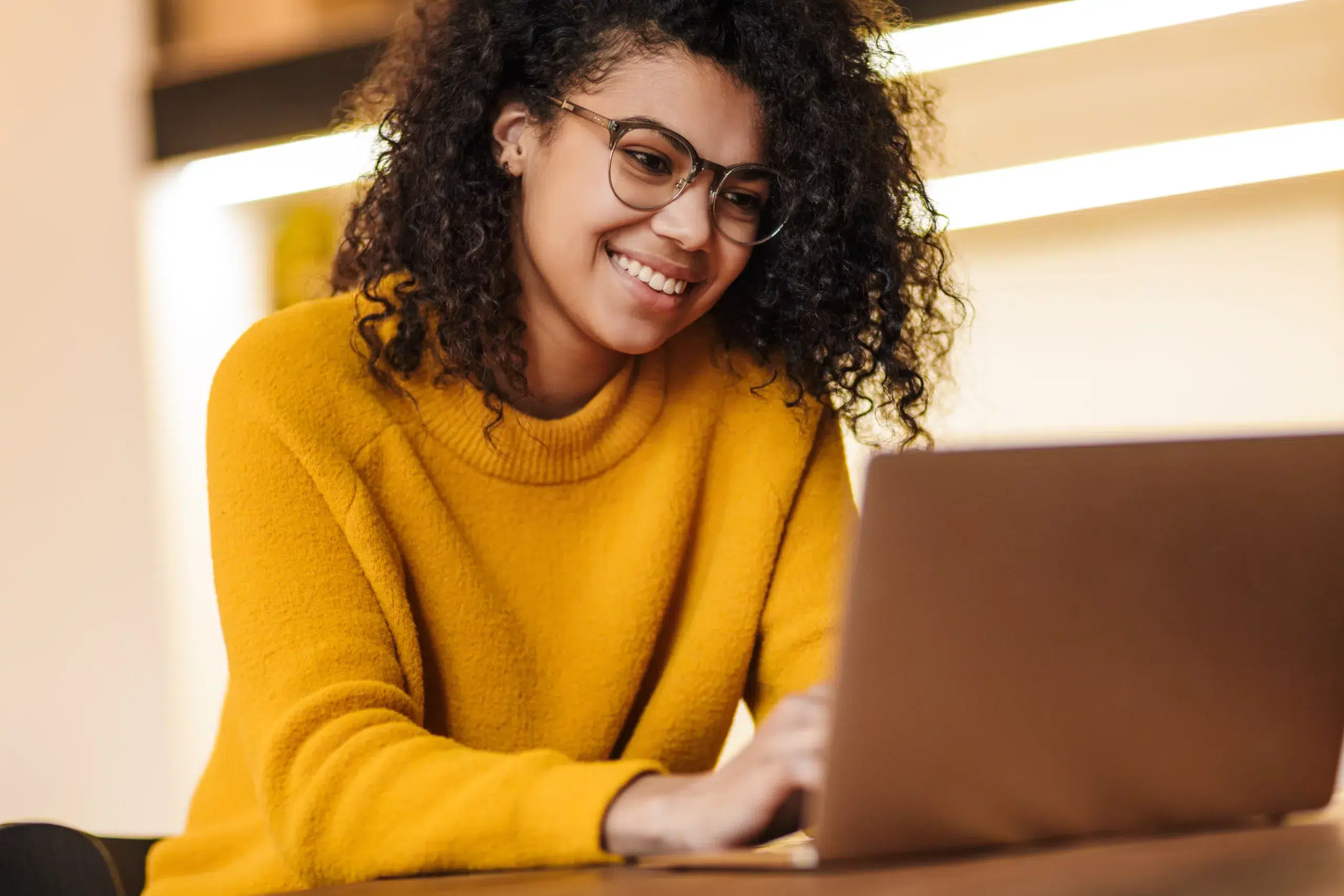 Image of cheerful african american woman in eyeglasses using lap