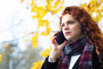 Serious woman speaks by mobile phone in the park outdoors in autumn.
