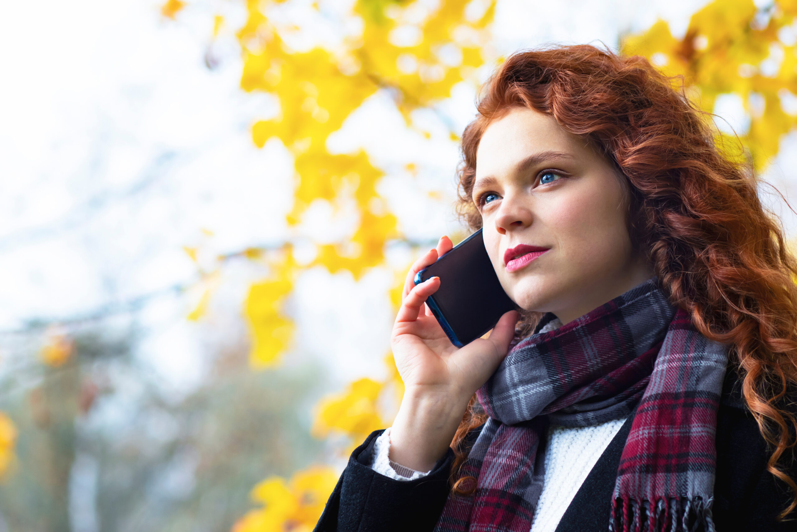 Serious woman speaks by mobile phone in the park outdoors in autumn.