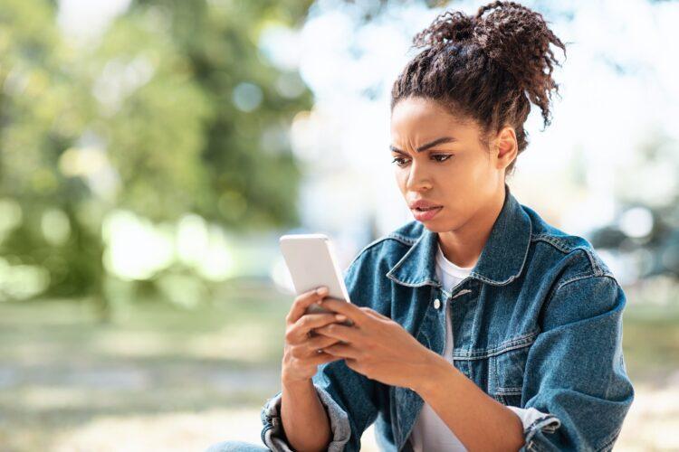 Displeased woman using smartphone while sitting outdoors