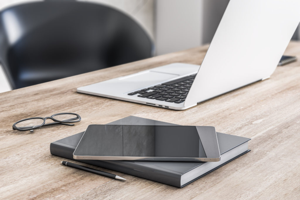 Modern digital tablet on wooden table surface with laptop, notebook and glasses.