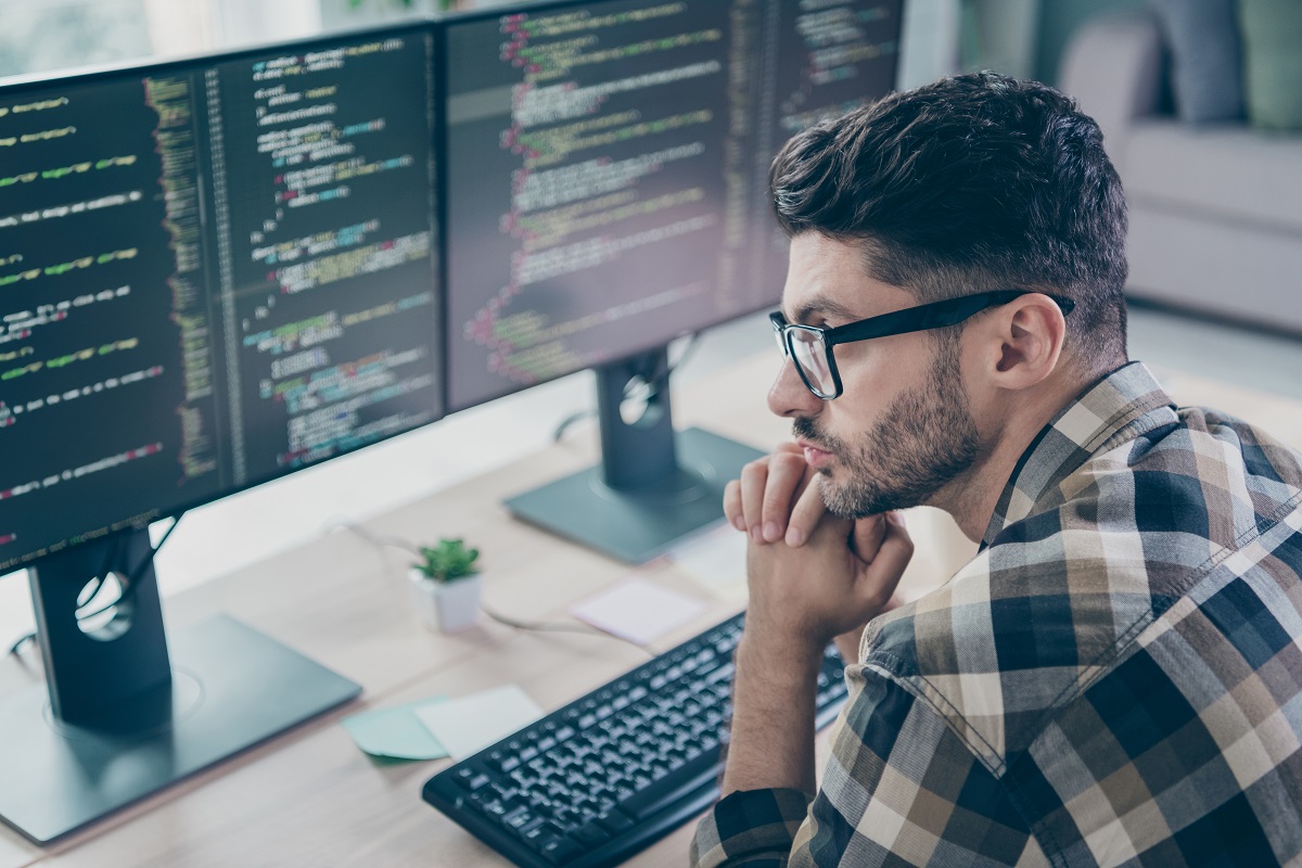 male programmer with glasses hands on chin in deep thought while looking at codes on screen