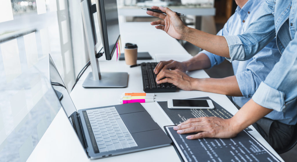 Programmers cooperating and working using desktop and laptop computers to code.