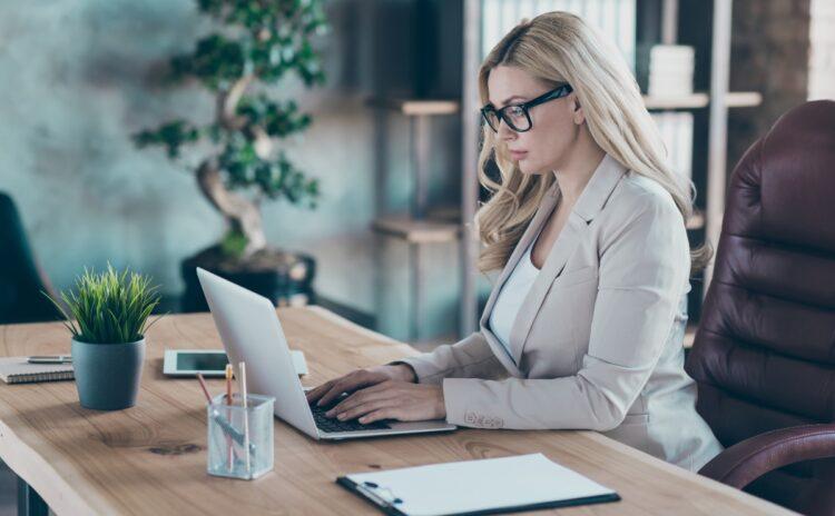 Blonde woman with glasses focused on her work on her laptop