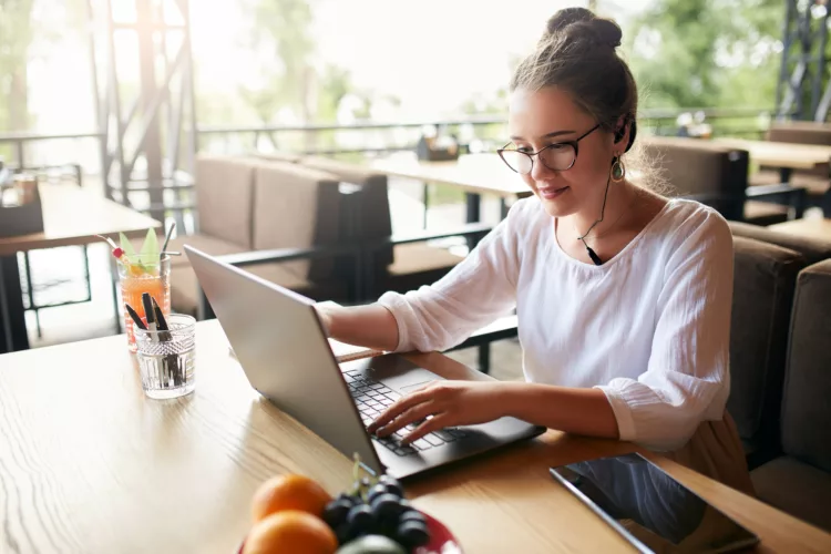 Woman working remotely at cafe with headset and laptop
