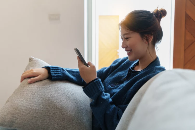 Young Asian woman using smartphone sitting on floor at bedroom. 
