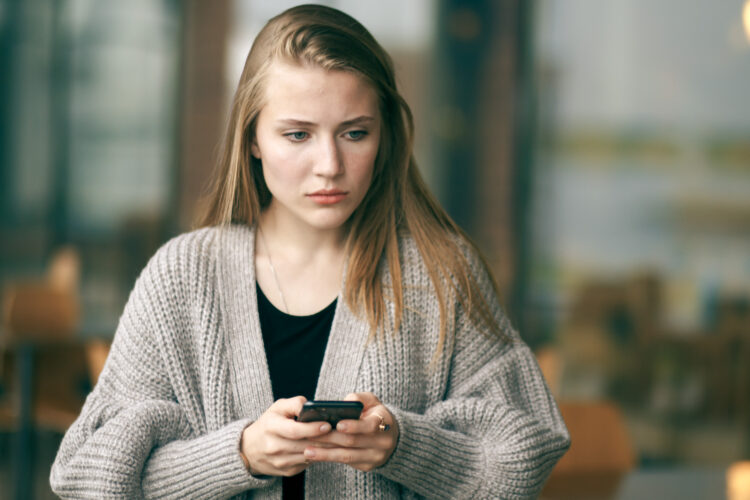 Young woman looking sad and worried while holding a cellphone.