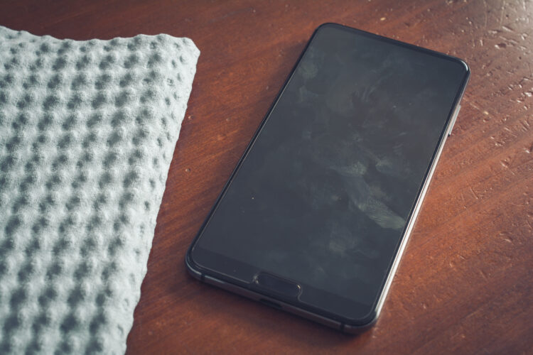 smartphone with dirty screen on wooden table next to a cloth