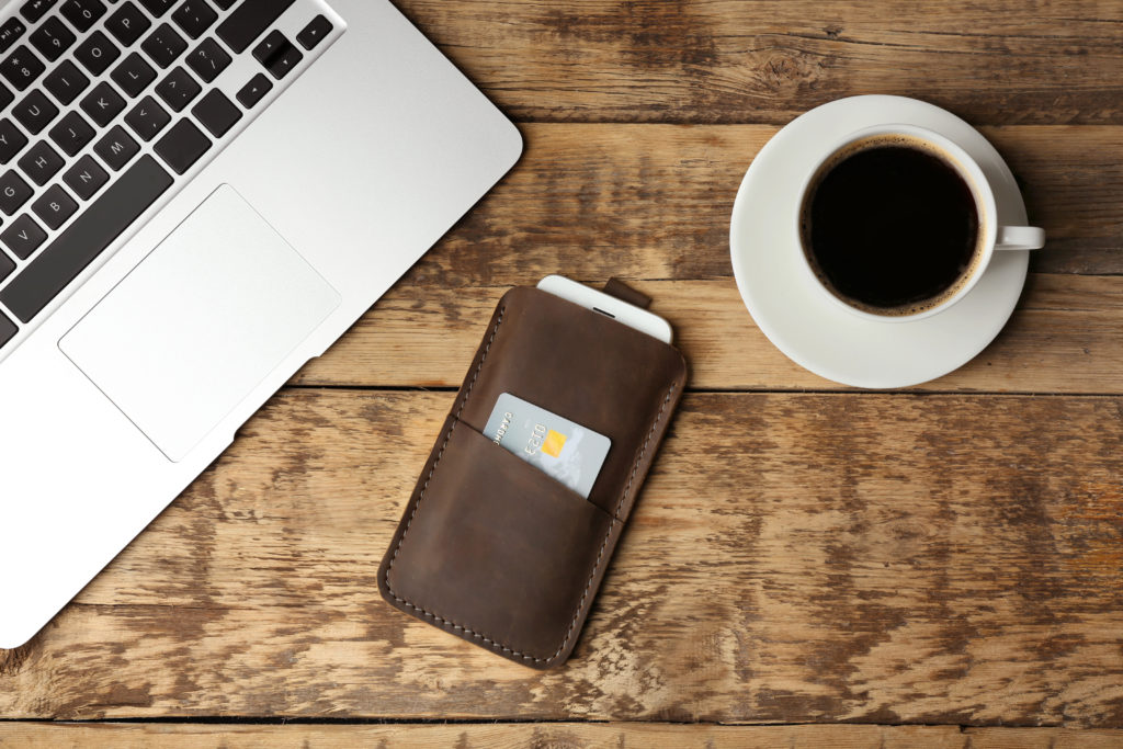 Leather case with mobile phone, laptop and cup of coffee on wooden table.