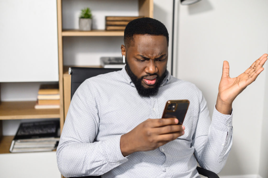 Guy in casual shirt holding his smartphone with a puzzled expression.