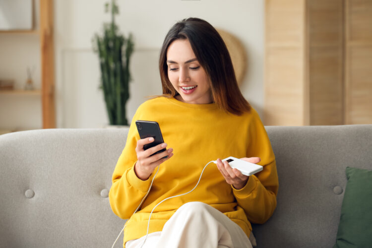 Young woman with phone and power bank at home