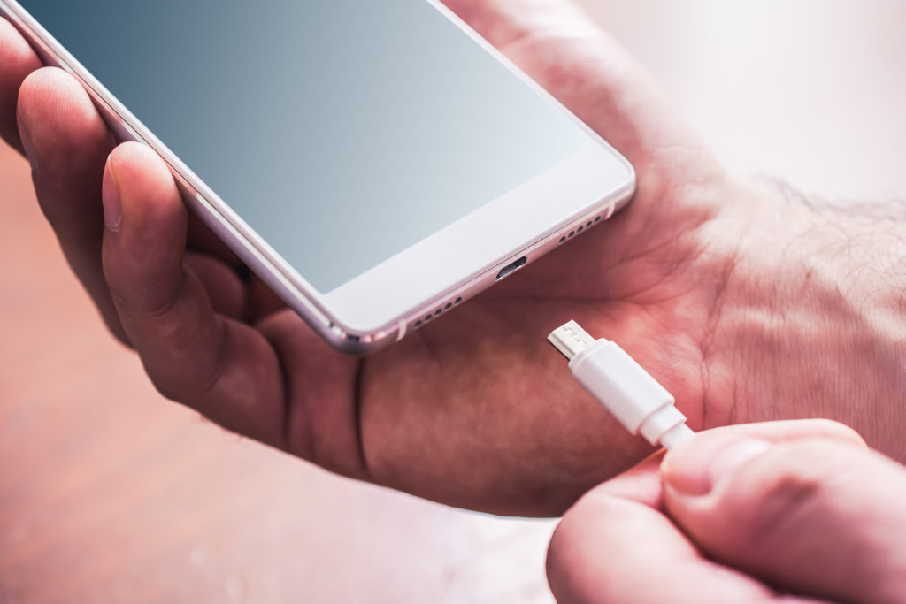 male hand removes power cable from mobile phone