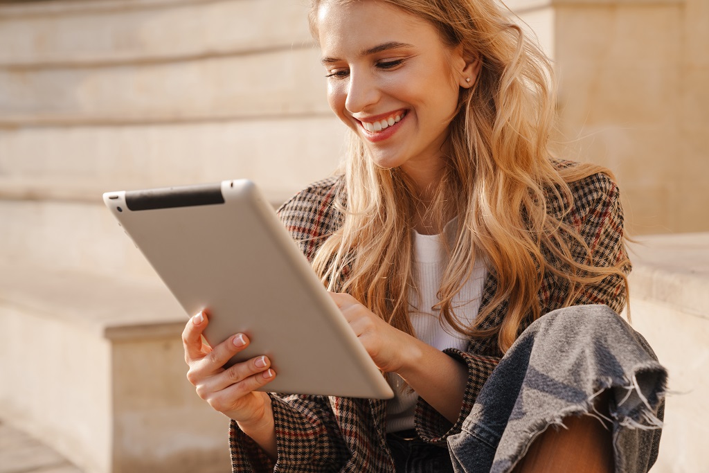 Smiling young blonde woman holding a tablet device indoors.