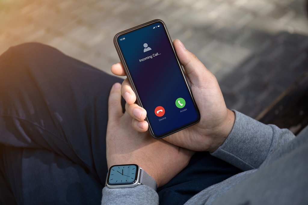 Male hands with watch holding phone with incoming call.