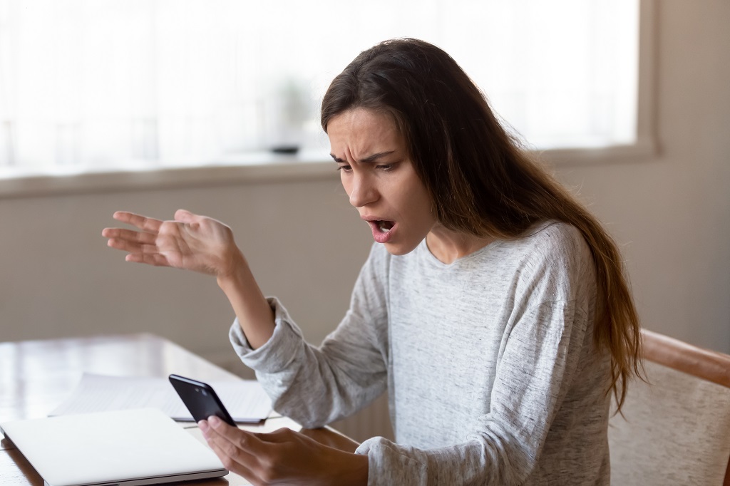 Angry young woman looking on mobile phone screen having problems.