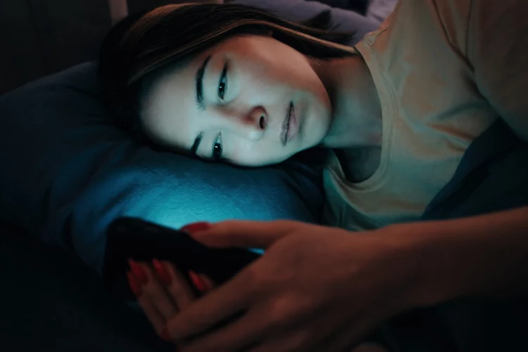 serious-looking woman uses the phone in bed at night.