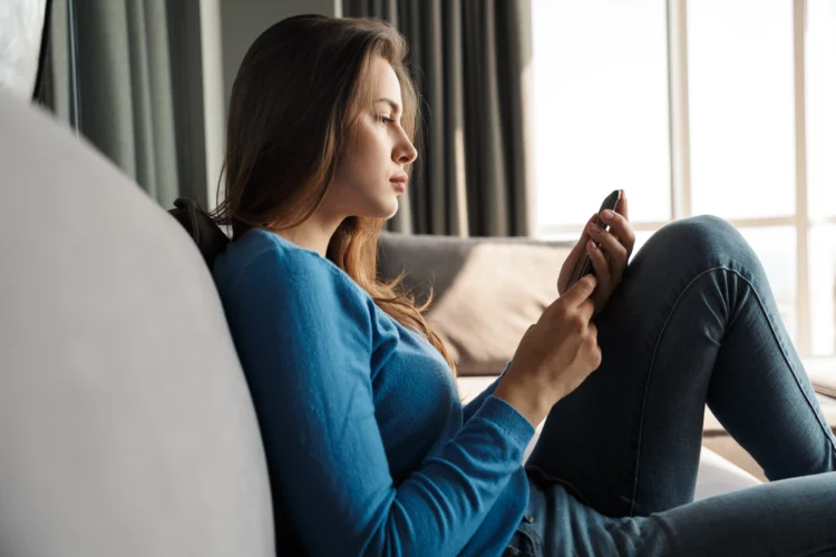 Young serious woman using mobile phone while sitting on the floor.