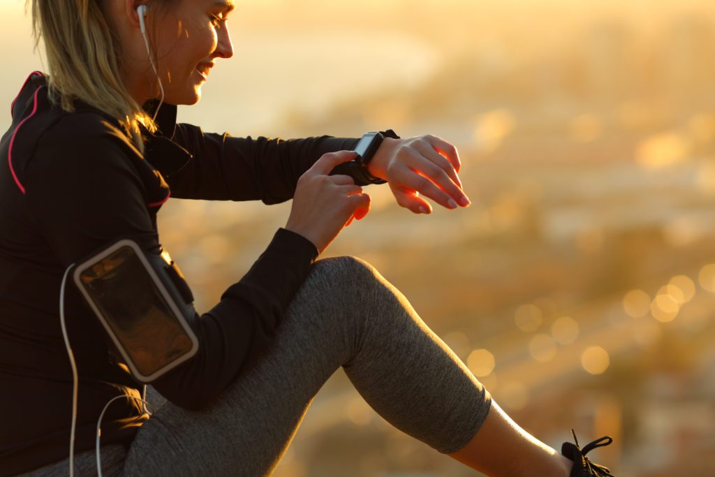 Runner with earphones resting and looking at her smartwatch.