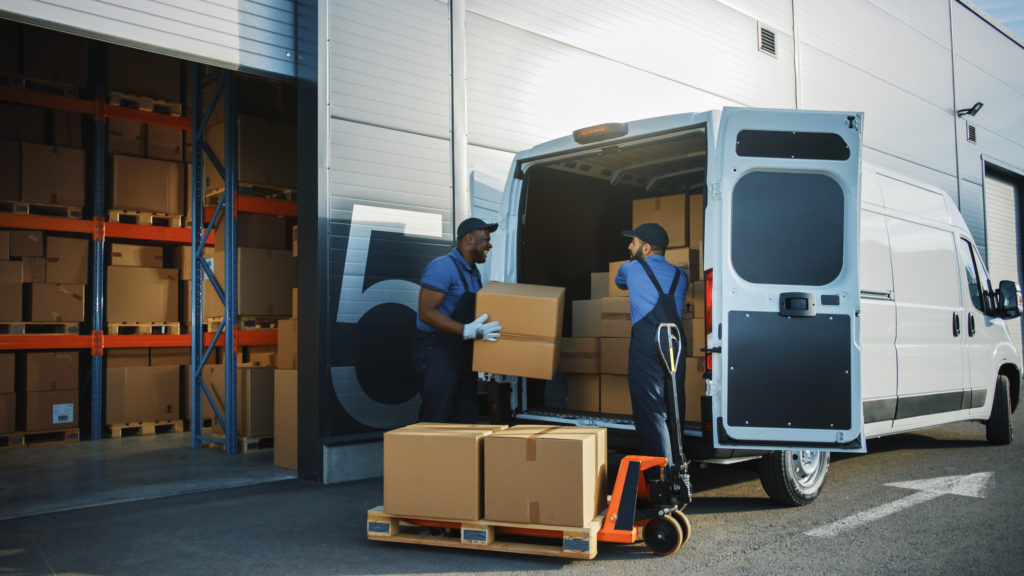 Outside of logistics distributions warehouse, workers loading delivery van with parcels.