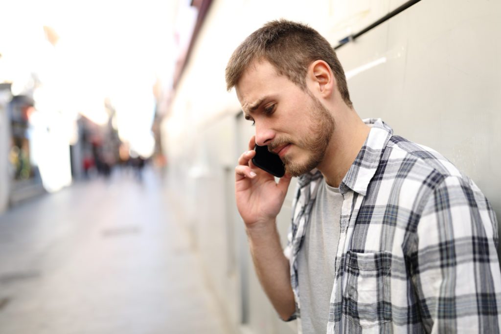 Sad man talking on a phone while alone on a street.