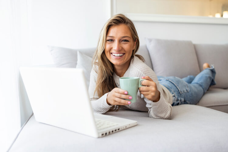 Woman using laptop at home, looking at screen smiling