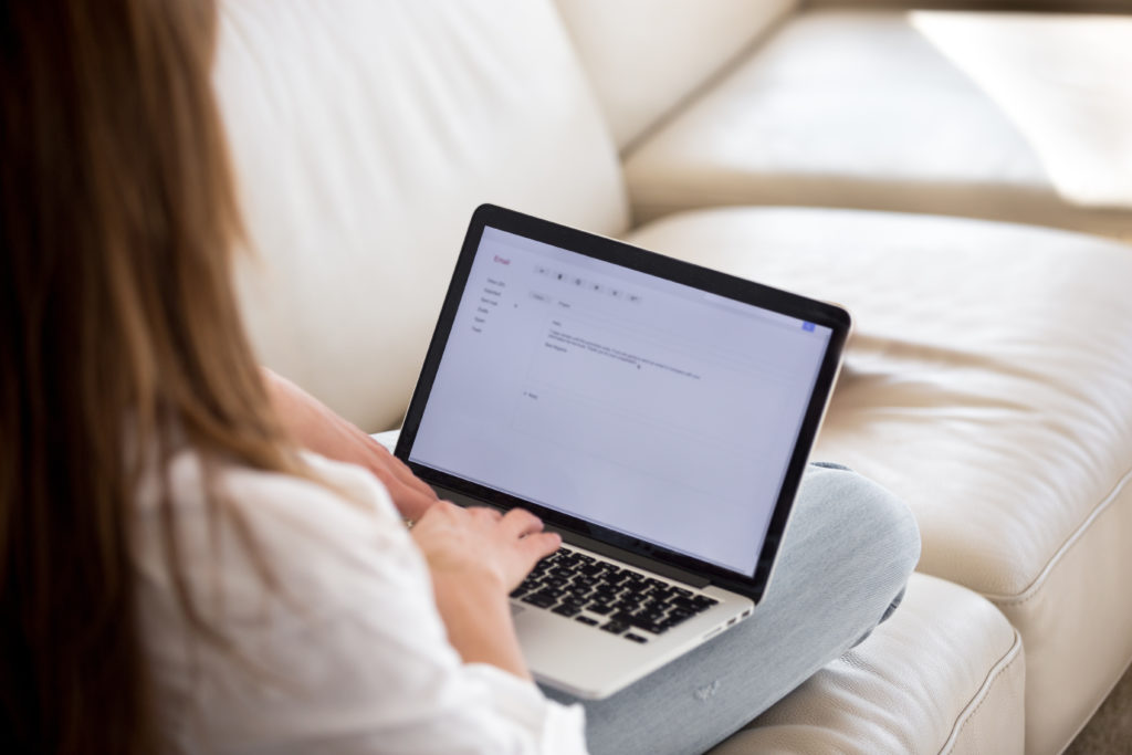 Rear view of woman writing email on laptop at home