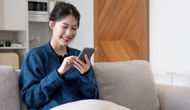Beautiful young asian woman use smart mobile phone on sofa