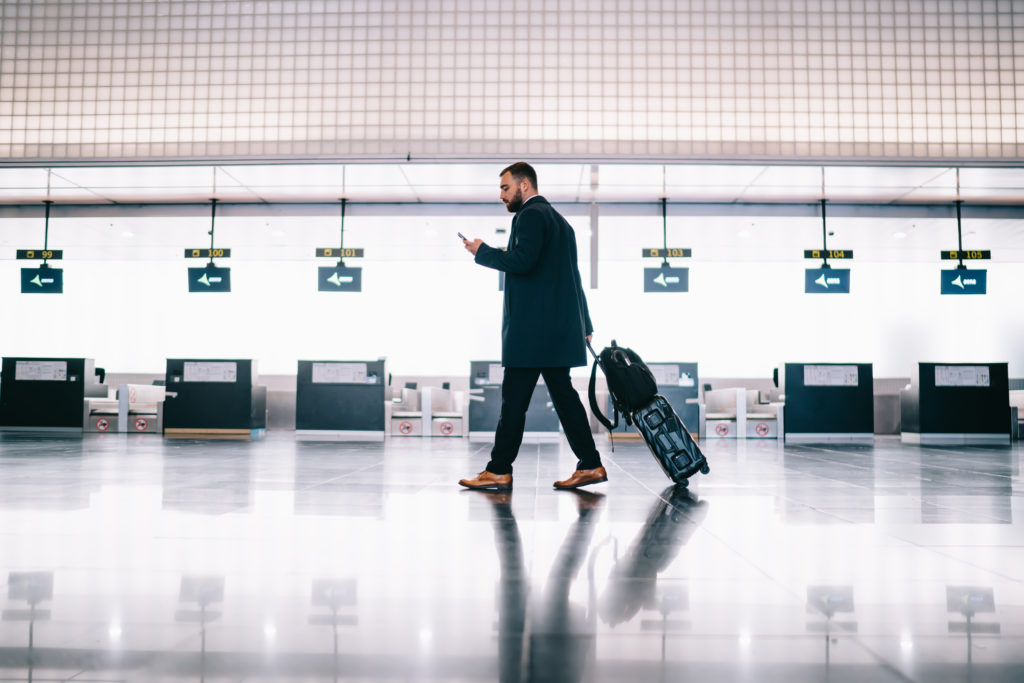 Businessman using cellphone while walking inside airport terminal.