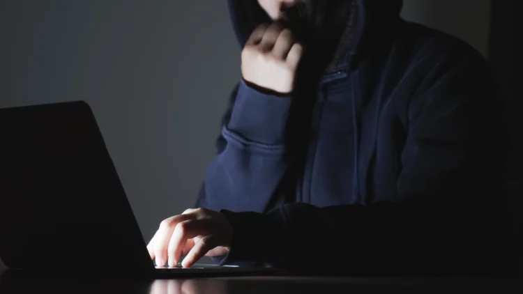 man in black hoodie doing suspicious stuff on laptop