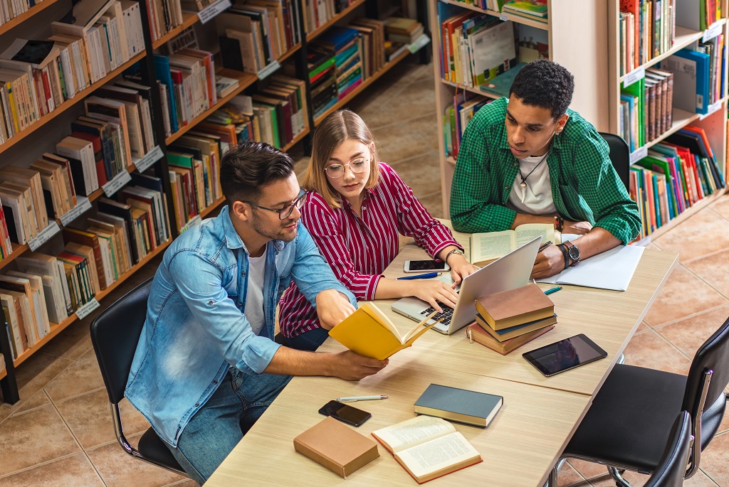 Three young students study in the school library and using laptop.