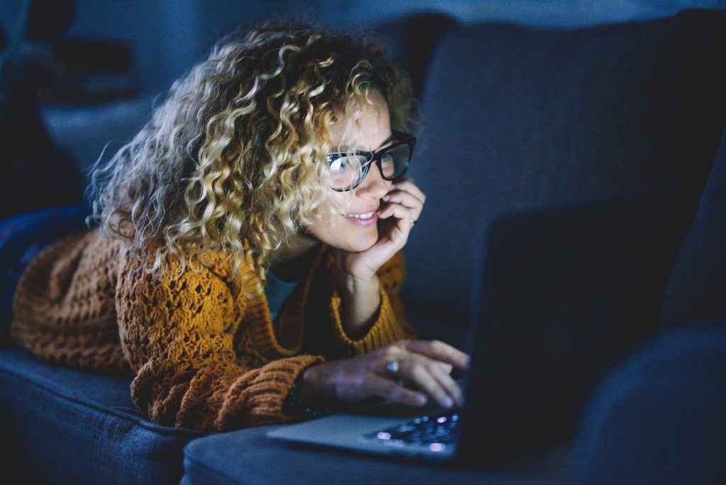 Woman uses her laptop computer at nighttime, bright LED reflects on her face.