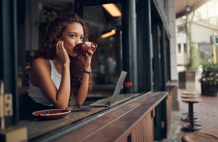 Young woman drinking coffee at cafe and focused on work with laptop. 