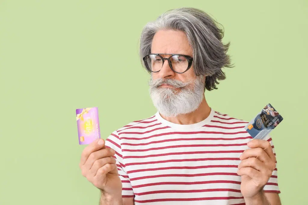 Senior man holding two gift cards, green background.