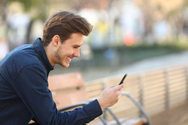 Happy guy using a smart phone in a park