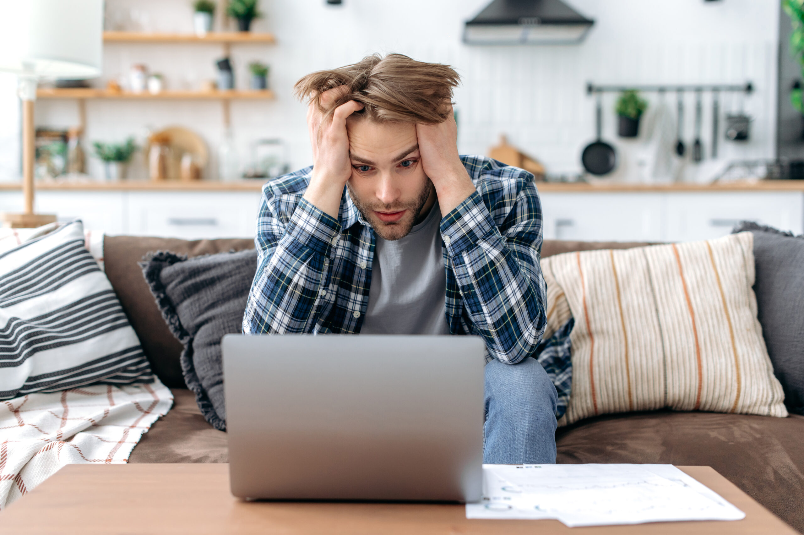 confused and upset young stylish man, sitting on sofa in living room, working online