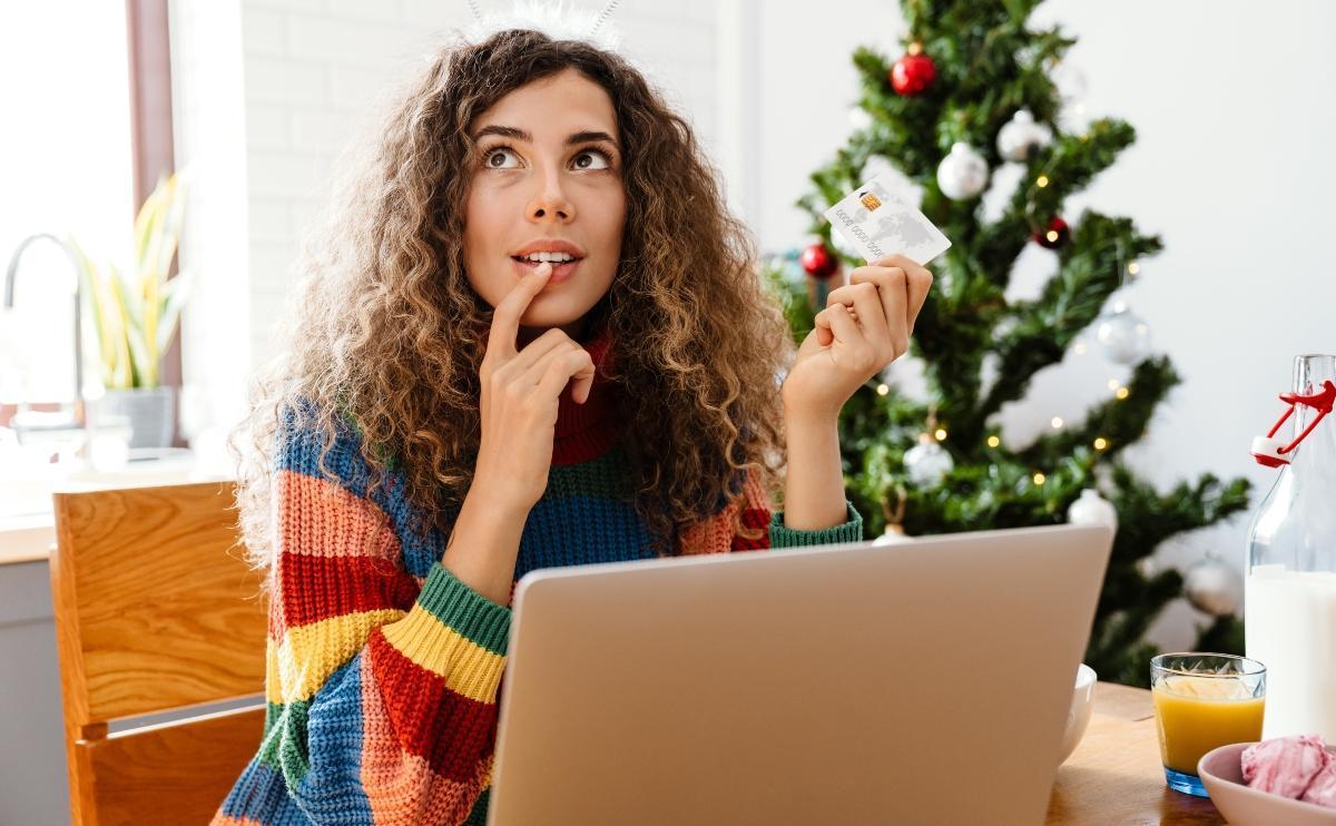 Woman in deep thought as she holds her credit card with the laptop open in front of her