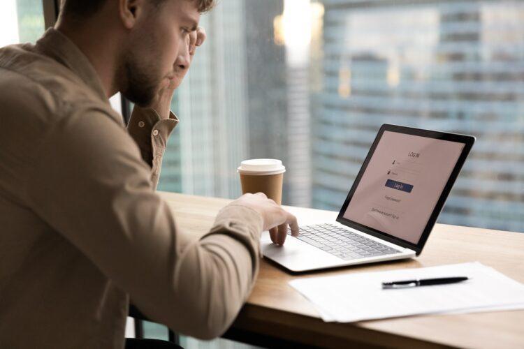 Young man sit by laptop about to enter personal account
