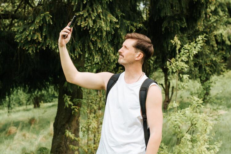 Man trying to catch signal on mobile phone outdoors in the forest.