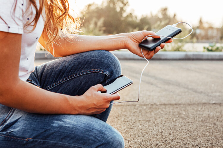 female hands holding black smartphone charging battery from power bank