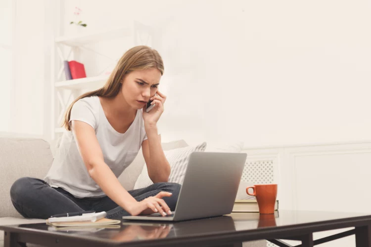 worried and frustrated woman on the phone while looking at her laptop