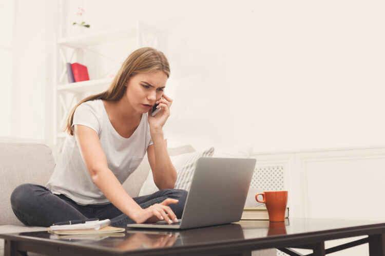 worried and frustrated woman on the phone while looking at her laptop