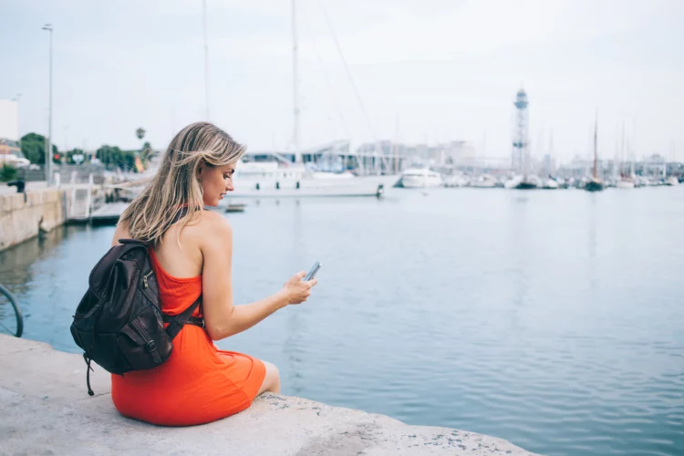 Pensive female traveler chatting on smartphone in port