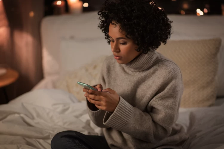 woman with smartphone sitting in bed at night